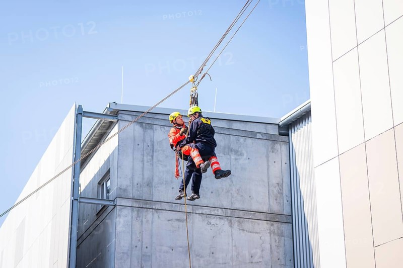 Two rescue workers in protective suits hang from a rope on the side of a building, Hospital Opening, Calw, Germany