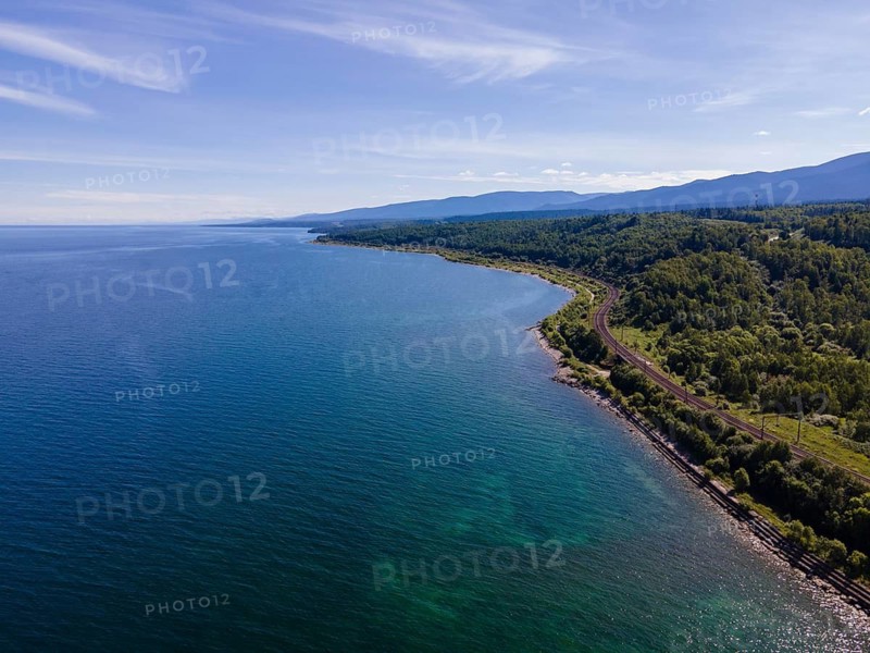 A beautiful coastal scene of Baikal, Irkutsk, Russia shows clear blue waters meeting a vibrant green terrain. The surrounding hills are rich with trees, creating a peaceful atmosphere ideal for nature lovers and outdoor activities
