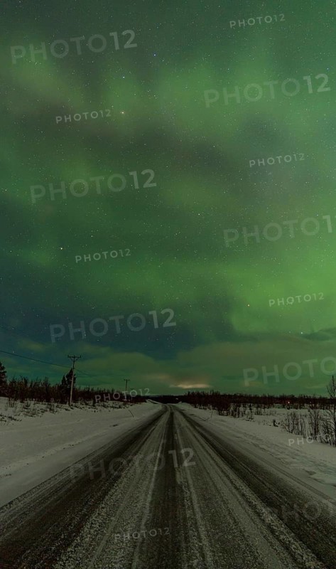 Stunning view of the Aurora Borealis illuminating the night sky with shades of green over a deserted, snowy road stretching towards the horizon in rural Kiruna, Sweden
