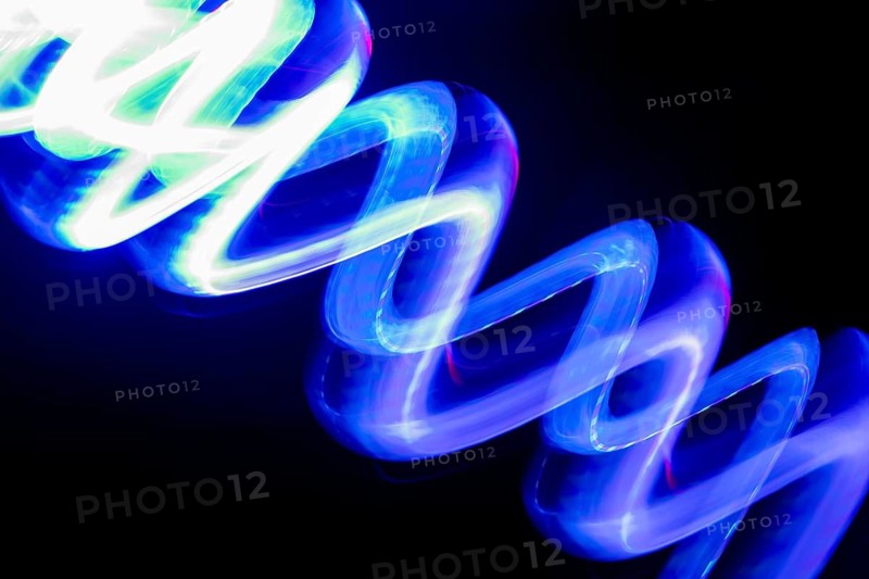 Vibrant blue neon light trails create dynamic patterns on a dark background. This long-exposure photography captures the mesmerizing movement of glowing abstract light art