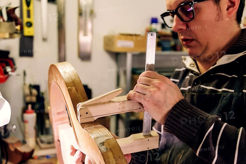 A luthier meticulously crafting a bass guitar in a workshop. The process showcases skilled craftsmanship, attention to detail, and passion for instrument making