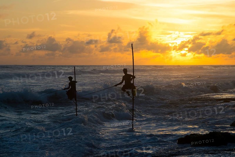 Silhouetted stilt fishermen practice their traditional craft against the backdrop of a breathtaking sunrise over the ocean in Sri Lanka, capturing a serene coastal scene