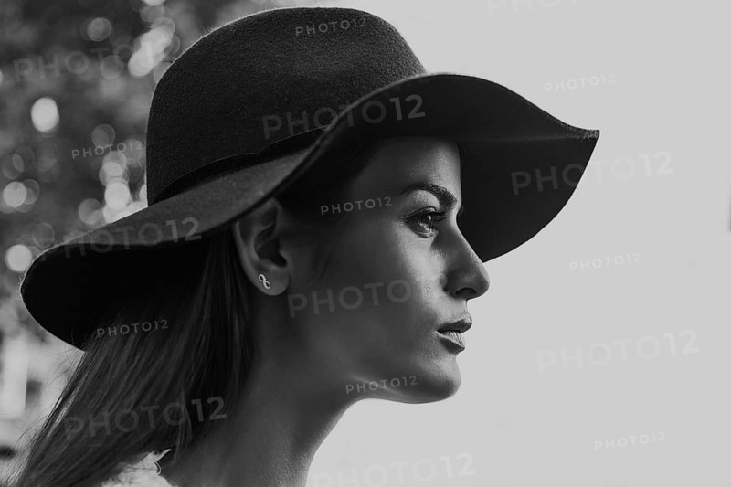 Black and white photo of a woman in profile wearing a wide-brimmed hat. The minimalist background highlights her timeless elegance and fashion-forward style