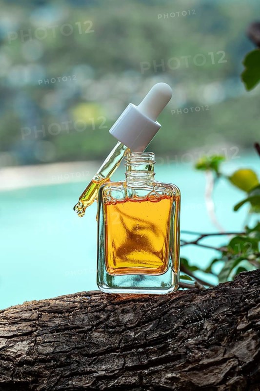 Luxurious cosmetic serum enriched with vitamins and golden particles, carefully positioned on a rich, textured tree bark against a serene seaside backdrop. The calm blue water enhances the elegance of the shimmering golden serum