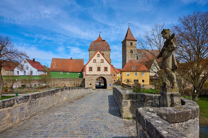 Stone bridge with statue and view of a village with church and historic buildings under blue sky, spring, Ornbau, Triesdorf, Franconian Lake District, Ansbach district, Middle Franconia, Bavaria, Germany