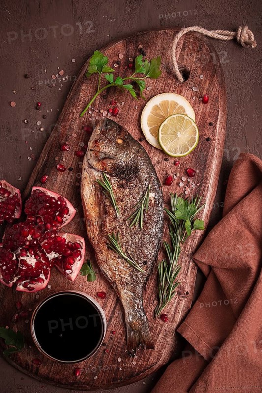 Fried dorado fish, with spices and herbs, on a wooden board, pomegranate sauce, close-up, no people