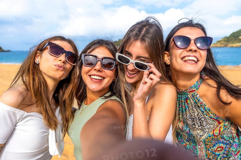 Four cheerful young women enjoying their summer beach vacation, smiling and posing for a close up selfie, celebrating friendship and good times together