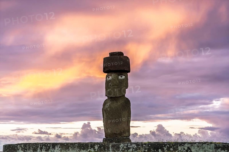 Moai statue Moai de la Paz with pukao and wise eyes on stone platform against cloudy sky at sunset, Ahu Ko Te Riku, Tahai, Easter Island, Chile