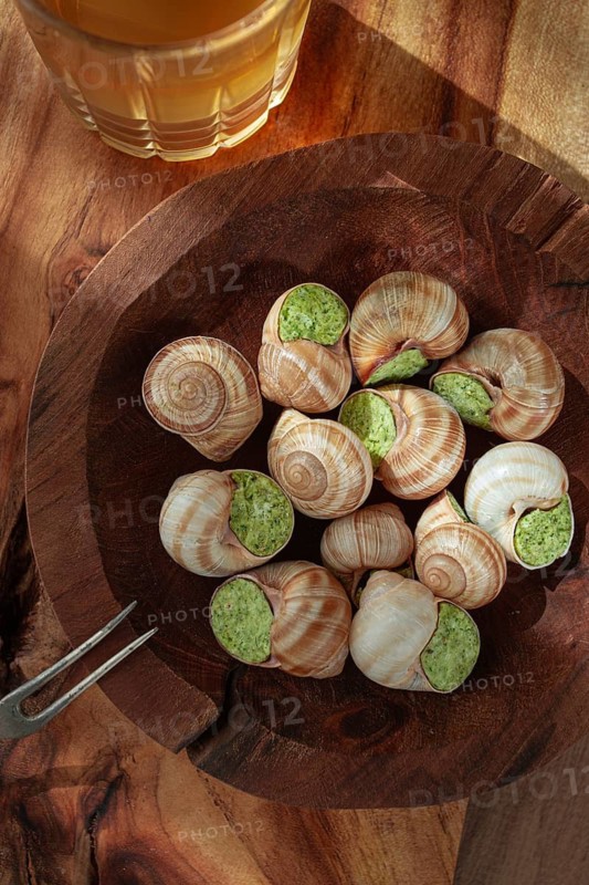 Snails cooked with herb oil on a wooden plate, served with white wine, natural light, no people