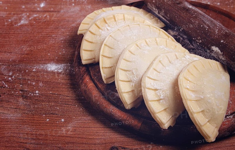 Raw chebureks, mini, on a cutting board, wooden table, close-up, no people