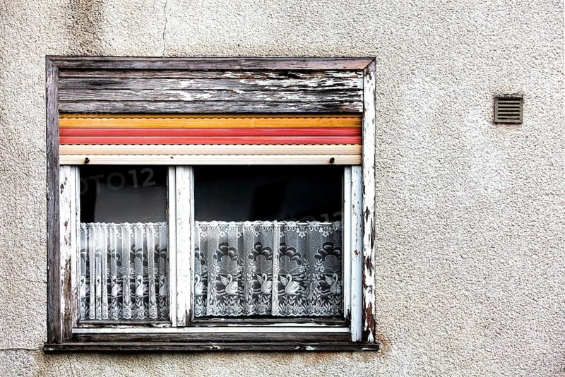 Old house facade, window with broken roller shutters and shabby curtains, Germany