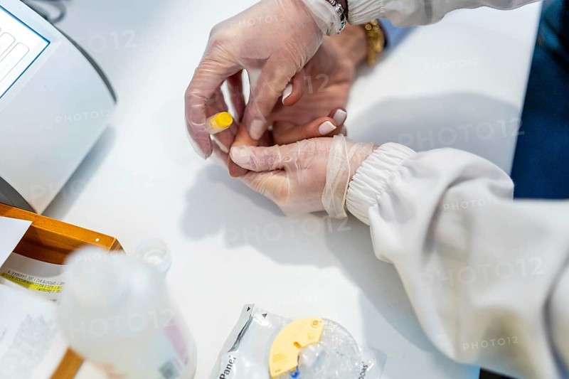 Healthcare professional wearing sterile gloves performing a rapid blood test using a lancing device on a patient's finger in a modern pharmacy setting, ensuring quick and accessible health screening