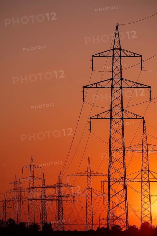 Silhouette of several high-voltage power lines and electricity pylons against a glowing orange and red sunset sky in Germany