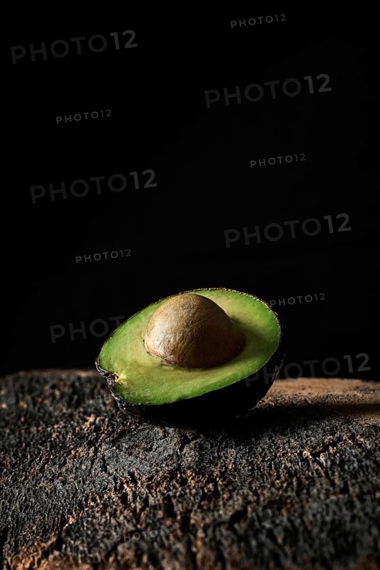 Half of ripe avocado with seed placed on rough surface against black background