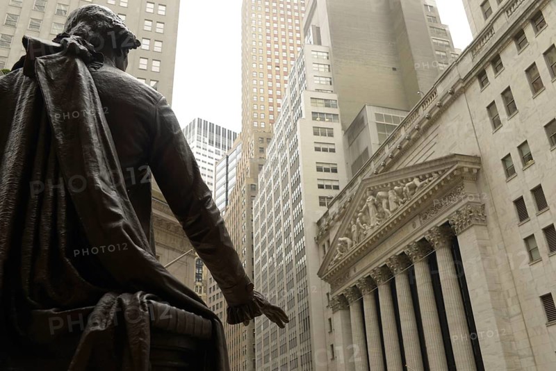 View from behind the George Washington statue at Federal Hall, looking towards the iconic New York Stock Exchange building adorned with classical columns and sculptures in Manhattan
