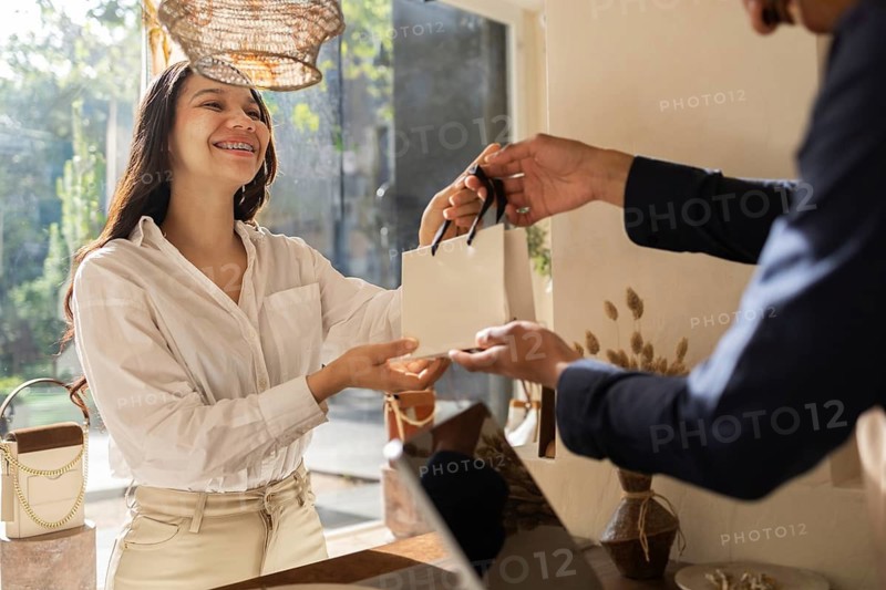 A cheerful customer receives a shopping bag from a sales associate in a sunlit bag store. The interaction highlights friendly service and a welcoming shopping environment