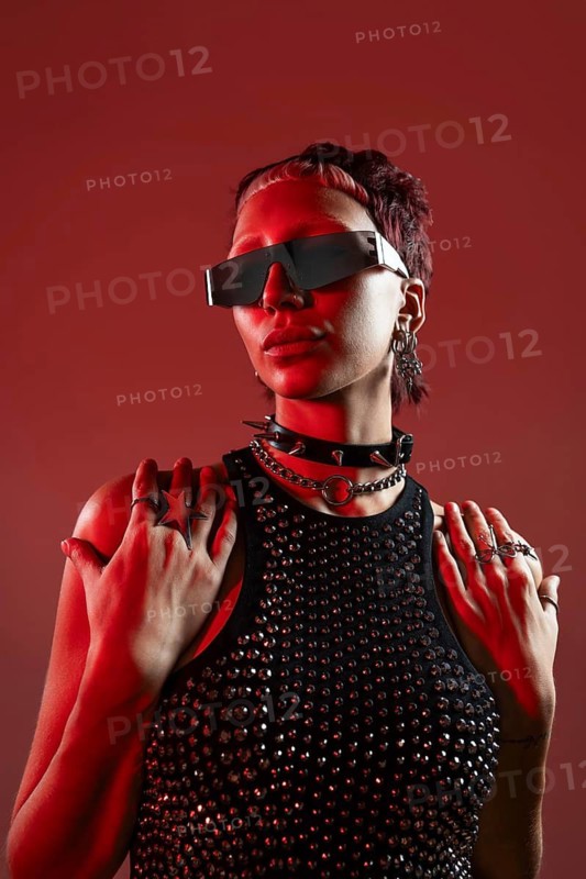 Cyberpunk-inspired female model in futuristic attire, adorned with industrial accessories and edgy makeup. The background glows in vibrant red hues, creating a striking visual impact