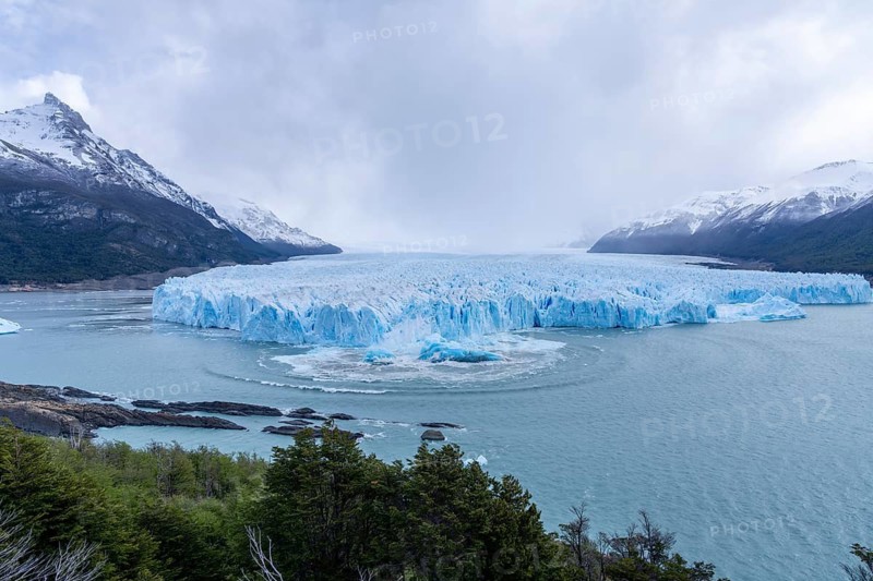 Perito Moreno glacier with calving event, rising ice block and wave rings in the water of Lake Argentino, surrounded by snow-capped mountains, Los Glaciares National Park, Santa Cruz Province, Patagonia, Argentina
