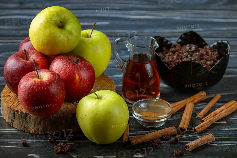 Combination of apples, cinnamon sticks and raisins next to a glass carafe with rum