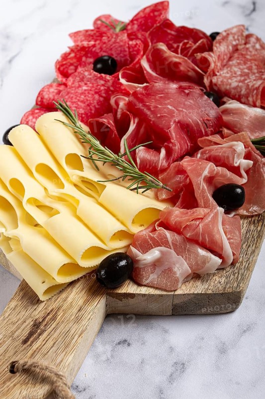 Assorted meat, appetizer, prosciutto, salami and ham, with maasdam cheese and olives, on a wooden board, breakfast, top view, close-up, no people
