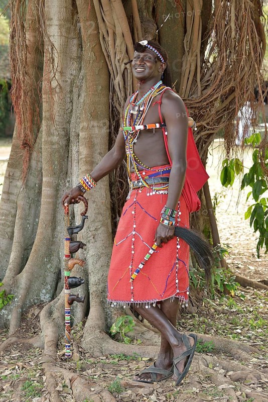 Maasai warrior wearing traditional dress and standing in a typical pose on one leg, near Enkutoto, Masai Mara, Rift Valley Province, Kenya