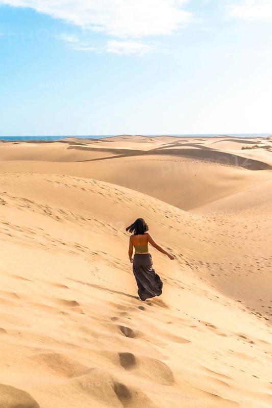 Tourist walking down the maspalomas dunes in gran canaria, spain, enjoying the sunny desert landscape