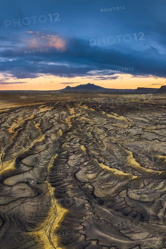 Sunset casts vibrant hues over the intricate, erosion-carved landscape of Factory Butte in Utah, highlighting the rugged terrain and vast expanses of wild earth