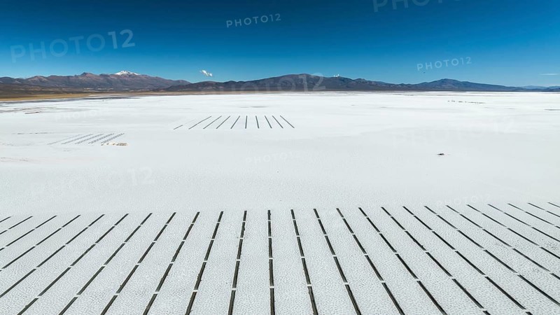 Expansive view of Salinas Grandes in Salta, Argentina. The white salt flats stretch towards the horizon, under a vast blue sky and distant mountain range backdrop