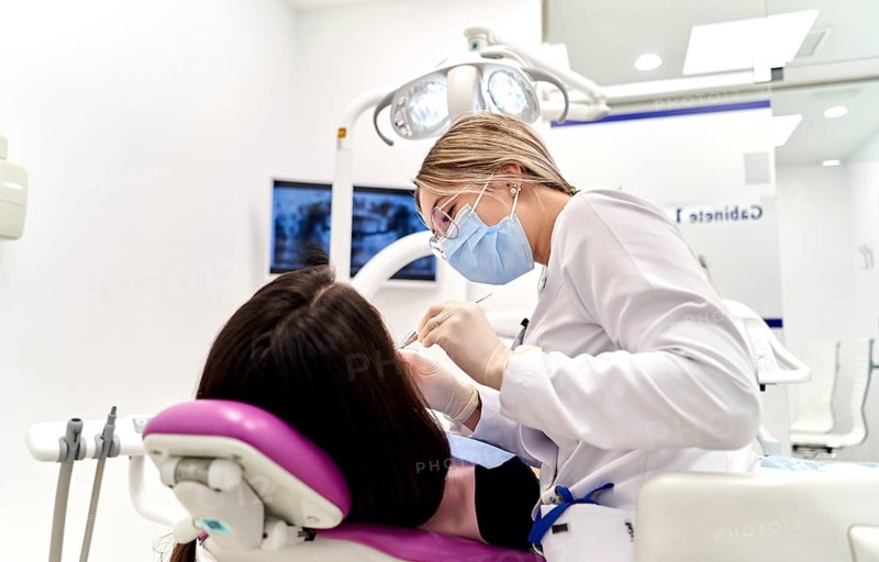 A dentist wearing protective gear attentively treats a patient in a modern dental clinic. The setting is clean and professional, reflecting a focus on hygiene and care