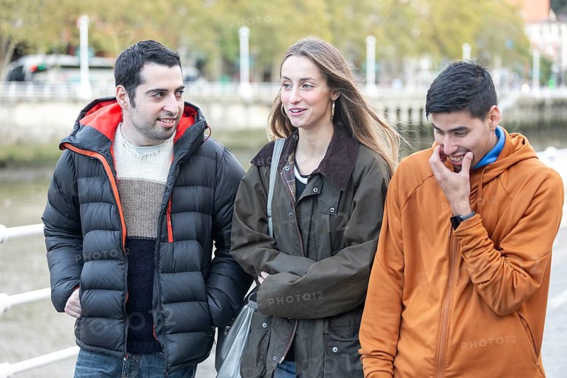 Caregiver walks alongside young men with intellectual disabilities, sharing a joyful conversation. Their smiles and relaxed expressions highlight inclusion and support in an urban setting