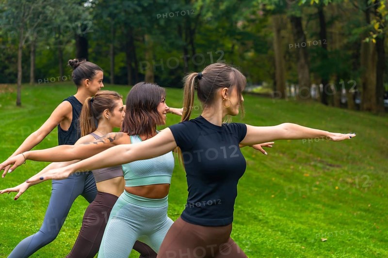 Group of diverse women practicing yoga in a park, performing a warrior pose in synchronization, focusing on wellness, fitness, and healthy lifestyle through outdoor exercise