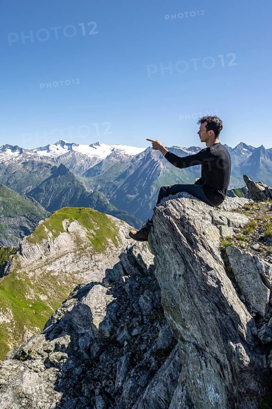 Mountaineer sitting on a rock, pointing to a mountain peak, mountain panorama with Großvenediger, mountain landscape with mountain peaks of the Venediger group, view from the summit of the Gösleswand, Lasörling group, Hohe Tauern National Park, East Tyrol, Tyrol, Austria