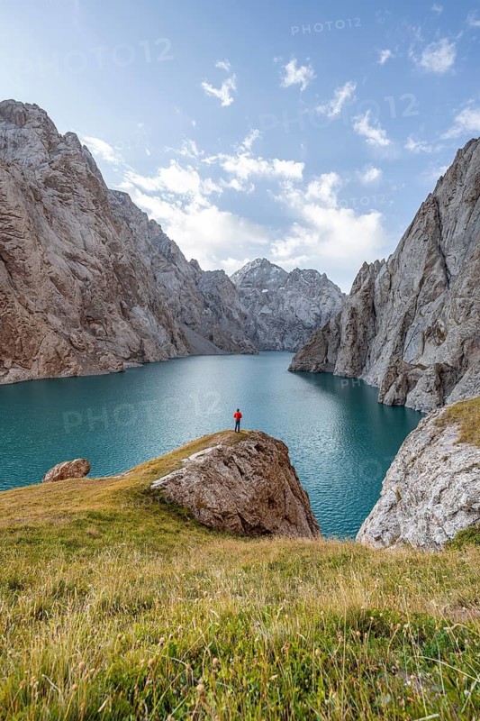 Tourist at the blue mountain lake between rocky steep mountain peaks, Kol Suu Lake, Sary Beles Mountains, Naryn Province, Kyrgyzstan