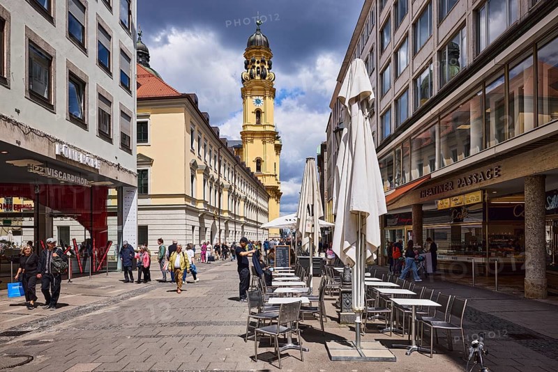 Church tower of the Theatine Church, St. Kayetan and Adelaide, Italian high Baroque style, general architecture, commercial building, pedestrian zone, outdoor area of a restaurant, confectionery and café Mälu, Fünf Höfe shopping center, shops, shopping, pedestrians as a secondary motif, blue sky, white and dark gray cumulus clouds, Theatinerstraße, Munich, state capital, district-free city, Bavaria, Germany