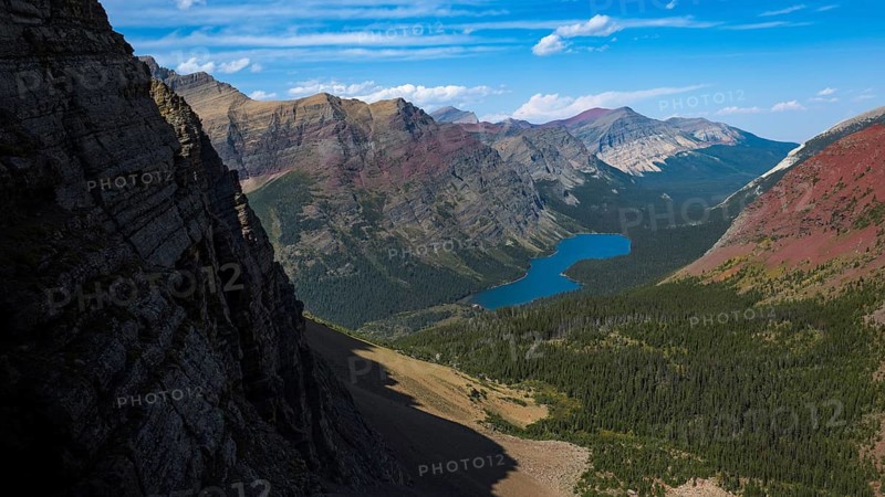 Stunning view of Glacier National Park, Montana, highlighting the rugged, mountainous terrain and lush greenery, with a pristine blue lake nestled among the peaks
