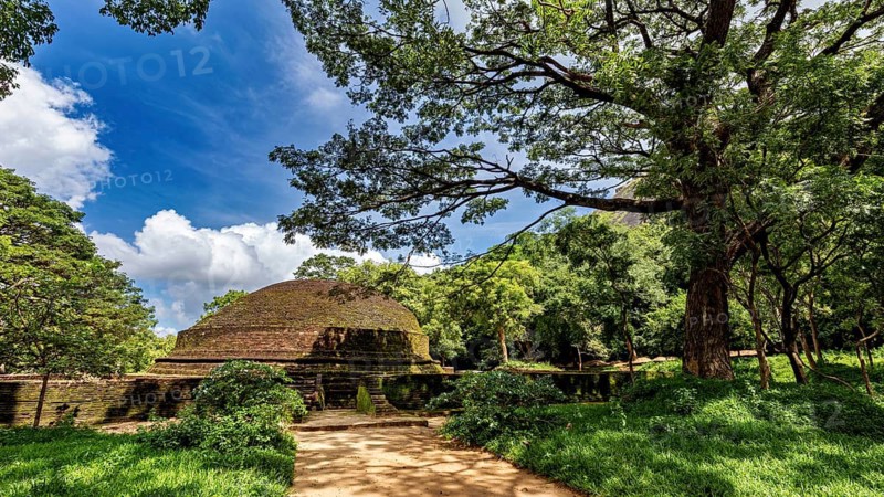 Ruins of an ancient stupa surrounded by lush greenery and a clear blue sky, temple ruins near Sigiriya in Sri Lanka