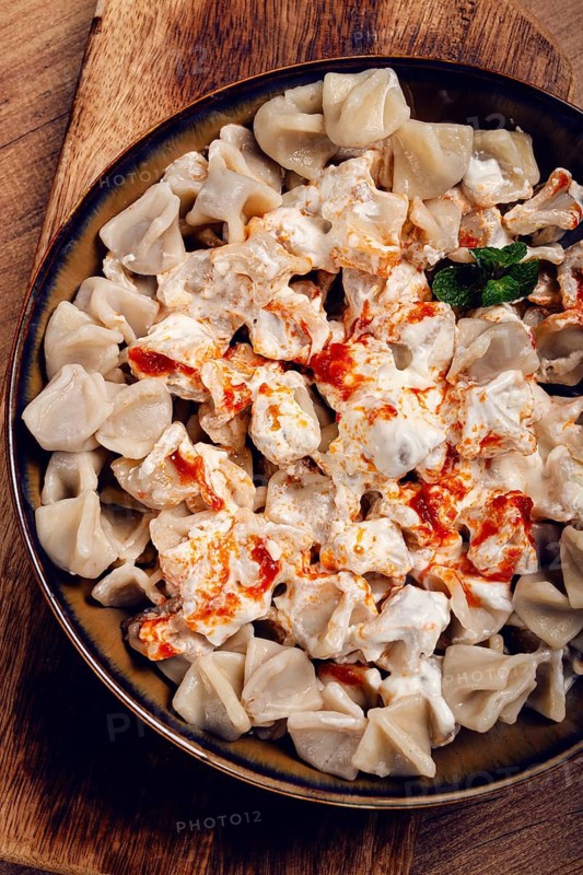 The dish features a generous serving of Turkish dumplings topped with velvety yogurt and a drizzle of spicy red sauce, .