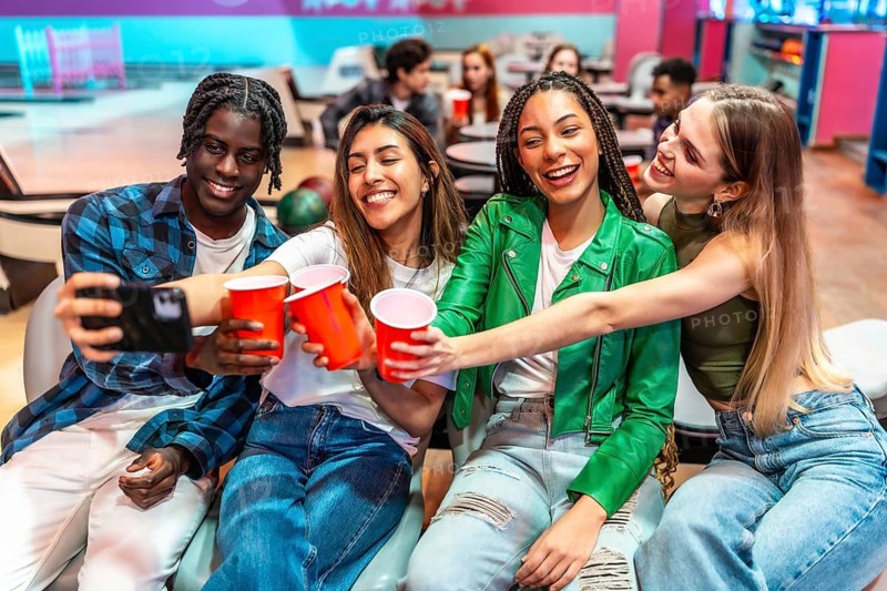Four multi ethnic young friends are making a toast and taking a selfie at the bowling alley, enjoying their weekend together