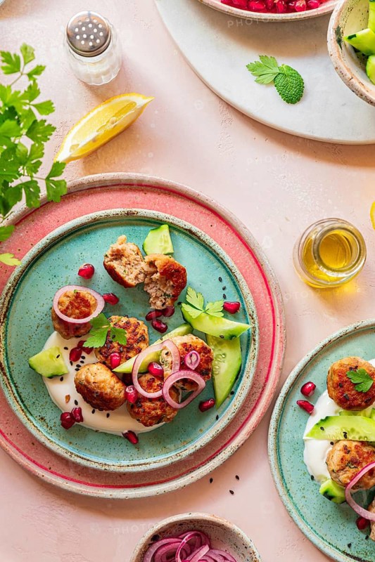 A vibrant Mediterranean meatballs dish on colorful plates, garnished with cucumber, onion, yogurt and pomegranate. Lemon and herbs add freshness, perfect for food concepts