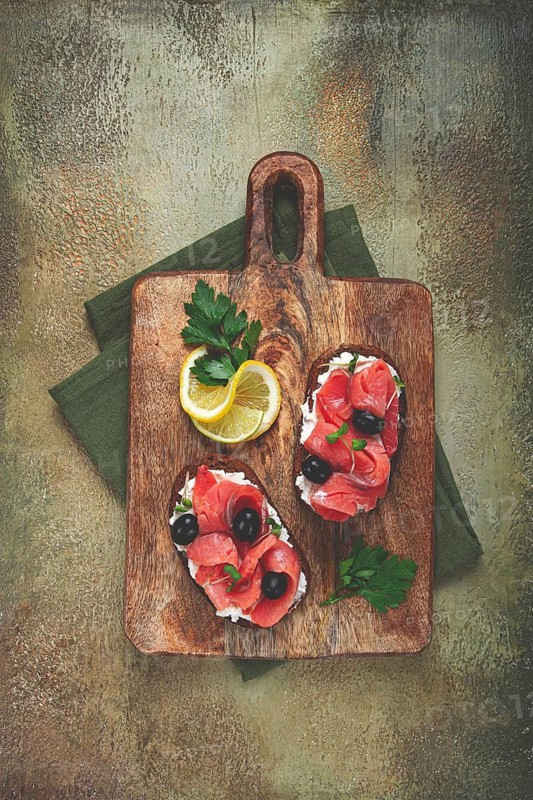 Sandwiches with cream cheese, chum salmon, cold smoked, grain bread, on a cutting board, top view, breakfast, lemon and parsley, no people