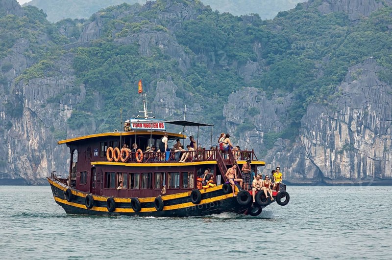 A traditional wooden boat with tourists sails through a rocky seascape, tourists on an excursion boat in Halong Bay in Vietnam