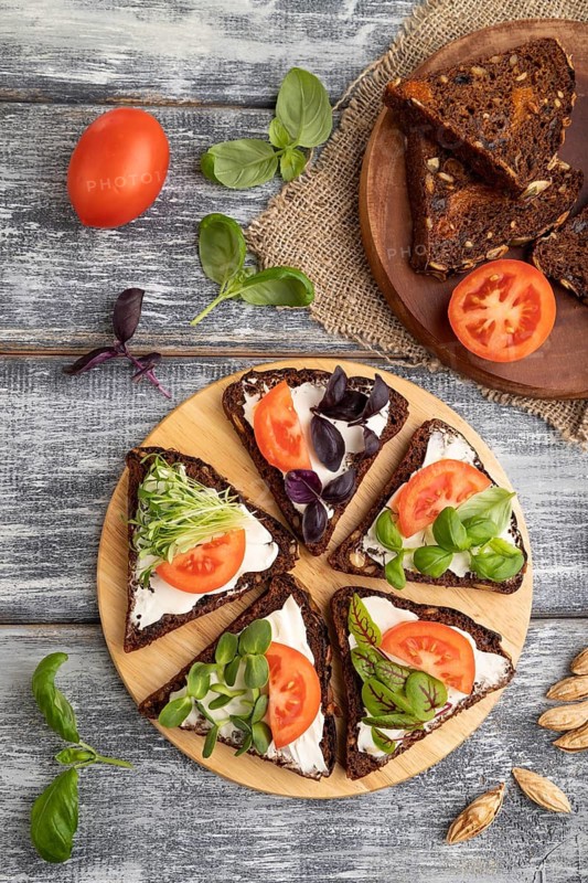 Grain rye bread sandwiches with cream cheese, tomatoes and microgreen on gray wooden background and linen textile. top view, flat lay, close up
