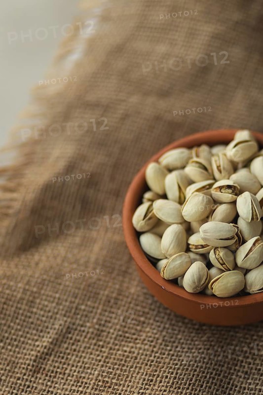 A terracotta bowl filled with pistachios rests on a rustic burlap fabric. The image highlights the earthy tones and natural textures, providing a warm, cozy atmosphere