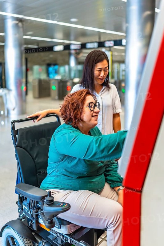 Vertical side view photo of a disabled woman and friend buying the ticket for the metro