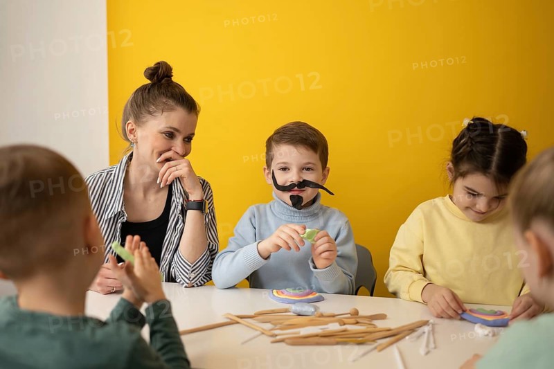 Children engaged in a lively art class, modeling clay, wearing playful costumes. They are enjoying a creative session with a teacher in a vibrant, fun environment