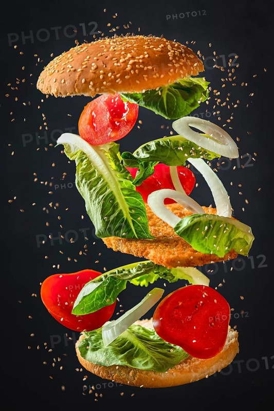 Ingredients of a burger with lettuce, tomatoes, onions and schnitzel floating freely on a dark background