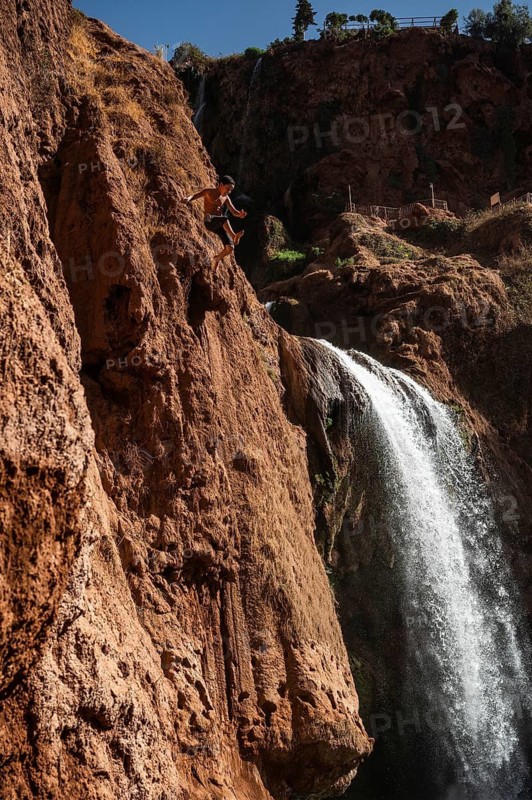 OUZOUD, MOROCCO - OCTOBER 5, 2024: A Moroccan young boy jumps from the high rock into the water under a waterfall Ouzoud