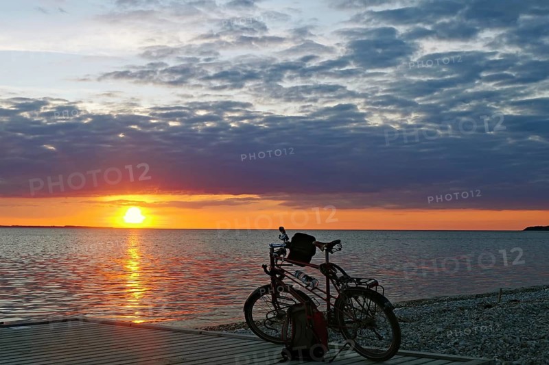 A bicycle is parked on the jetty as the sun sets over the sea in a colorful sky on the horizon