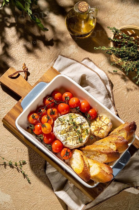 A delicious baked Camembert cheese served with cherry tomatoes and crispy bread in a vintage dish. Fresh thyme and roasted garlic add rustic charm to this gourmet appetizer