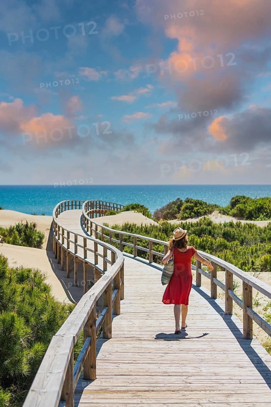 Girl with red dress on the wooden path to Playa Moncayo in Guardamar del Segura next to Torrevieja, Alicante. Community of Valencia. Spain, holidays in the Mediterranean